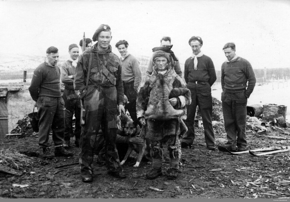 Midt på bildet John Edvin Aslaksen (1920-1995), som var soldat i den norske brigade, 2. bergkompani. Han var fra Porsanger, men gift i Karasjok. Han står ved siden av «stifinner og kjentmann» for soldatene, Per Nilsen Gaup (1916–2000) iført pesk, reingjeter i Børselv. Fotografert i Børselv vinteren 1944–45.
 Foto: Finnmark fylkesbibliotek digit